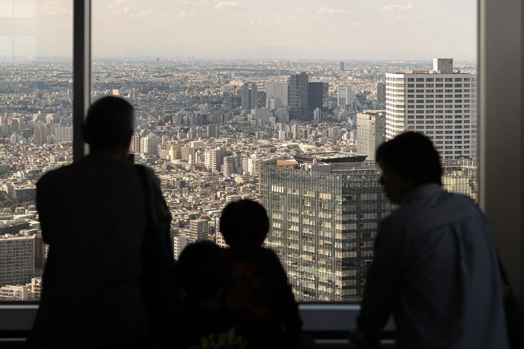 高層ビルの窓から街を見下ろす家族(自社株を家族の資産管理会社に移す事業承継のイメージ)